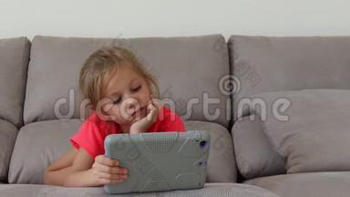 兴奋的小女孩躺在沙发上看动画片或看动画片时使用数码平板电脑的肖像